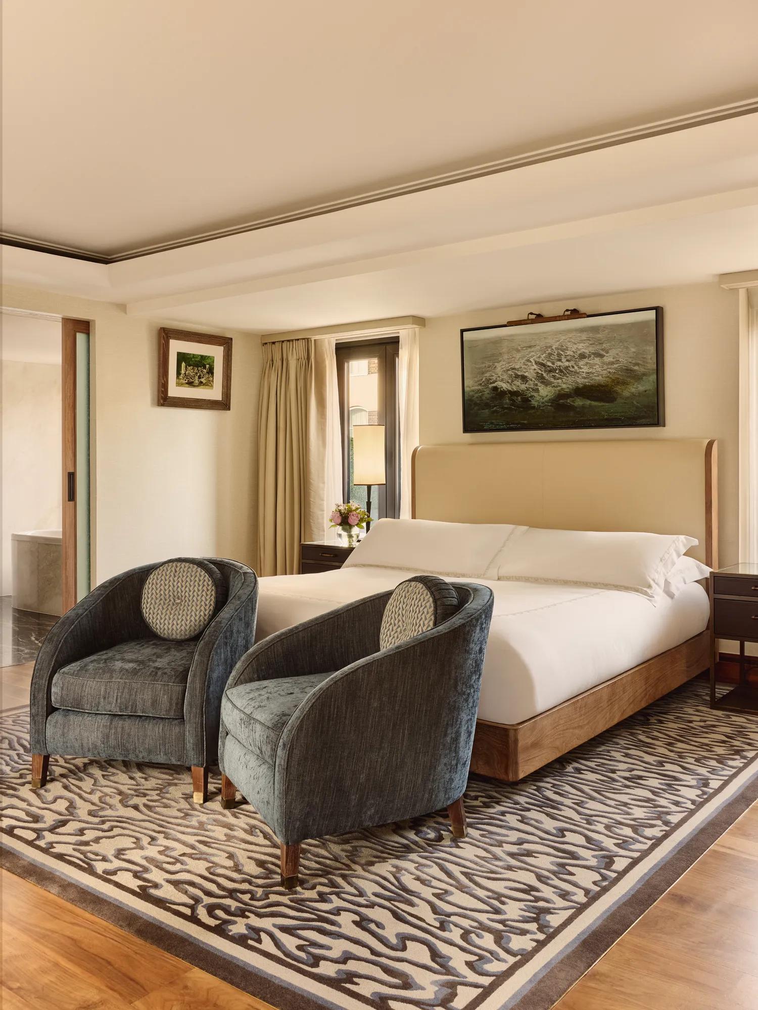 Luxury bedroom with upholstered bed, two velvet armchairs and patterned rug.