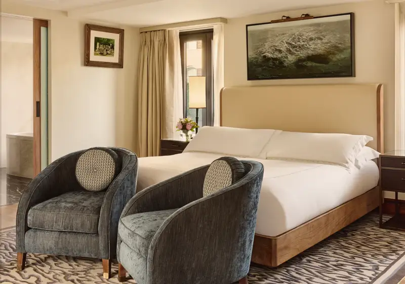 Luxury bedroom with upholstered bed, two velvet armchairs and patterned rug.