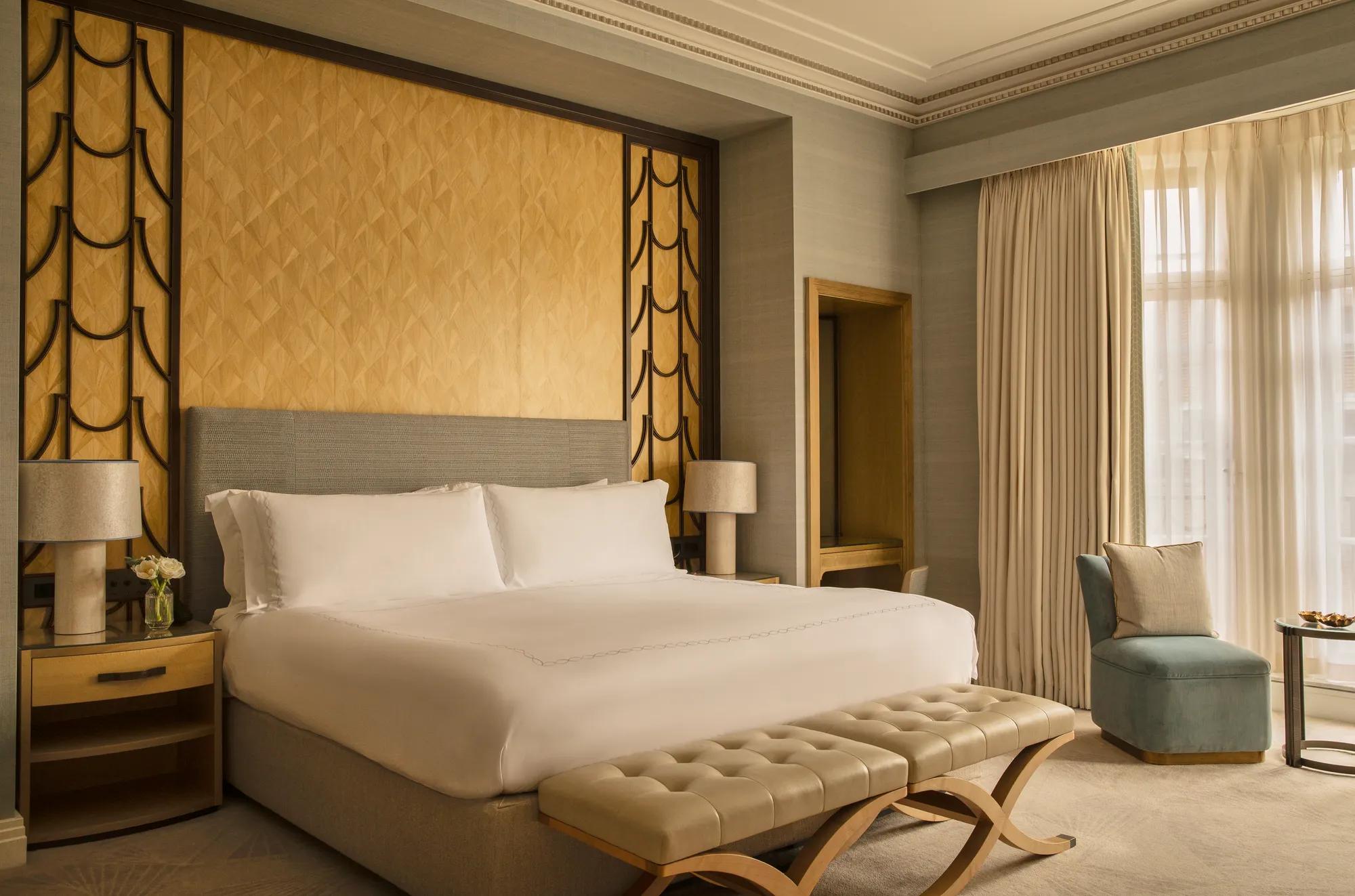 Contemporary bedroom with a king-size bed, upholstered bench and blue accent chair, set against a textured gold feature wall beside floor-to-ceiling windows.