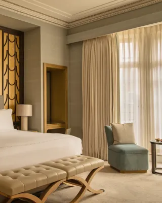 Contemporary bedroom with a king-size bed, upholstered bench and blue accent chair, set against a textured gold feature wall beside floor-to-ceiling windows.