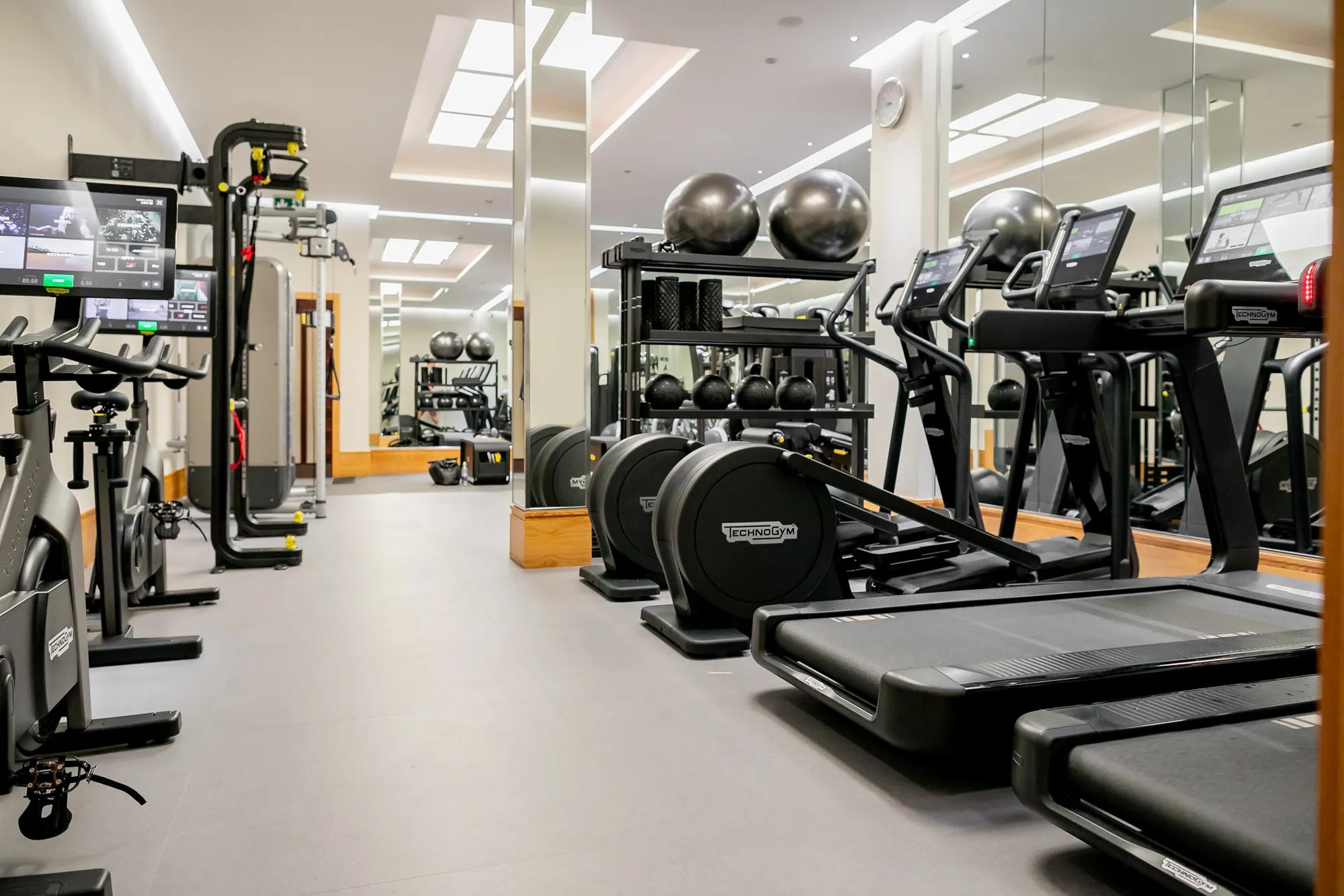 	Bright gym room featuring cardio machines, free weights, and open floor space for training.