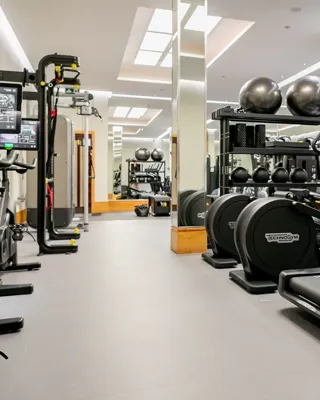 	Bright gym room featuring cardio machines, free weights, and open floor space for training.
