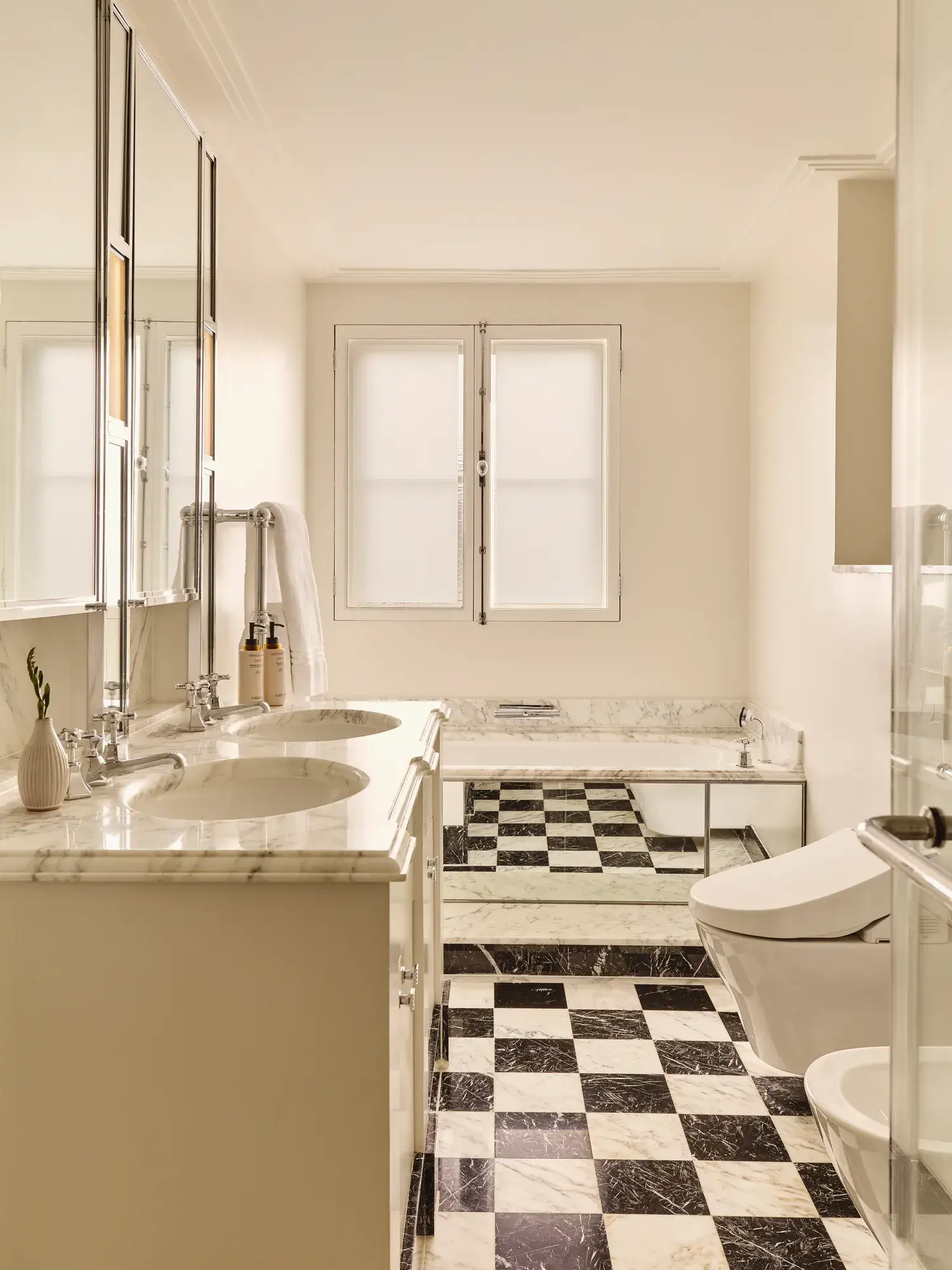 Elegant marble bathroom with double vanity, checkered floor, bathtub, and walk-in shower.