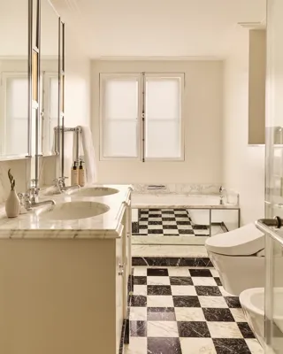 Elegant marble bathroom with double vanity, checkered floor, bathtub, and walk-in shower.