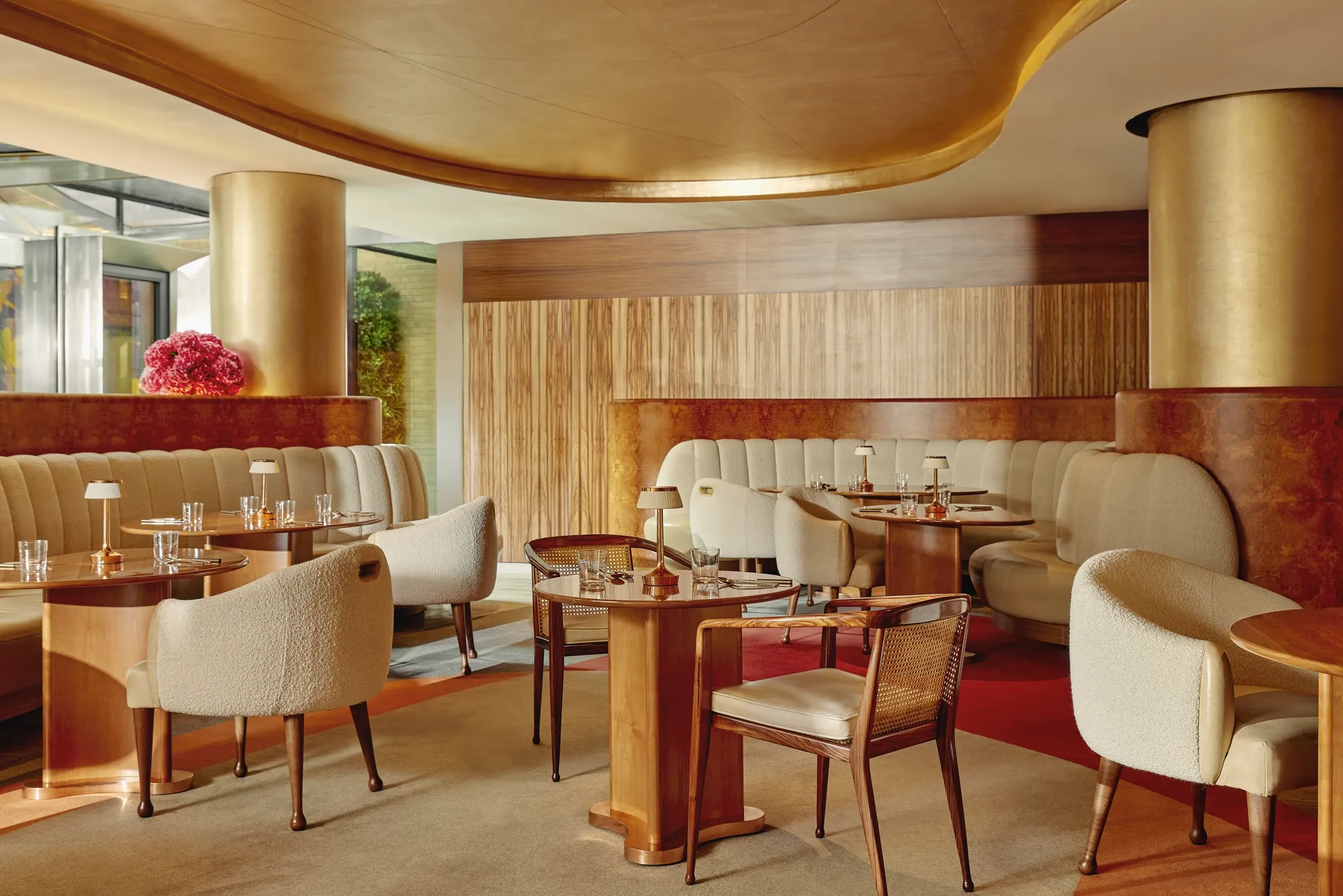 Warm, contemporary café with soft cream seating, wood accents, gold finishes, and intimate table settings.