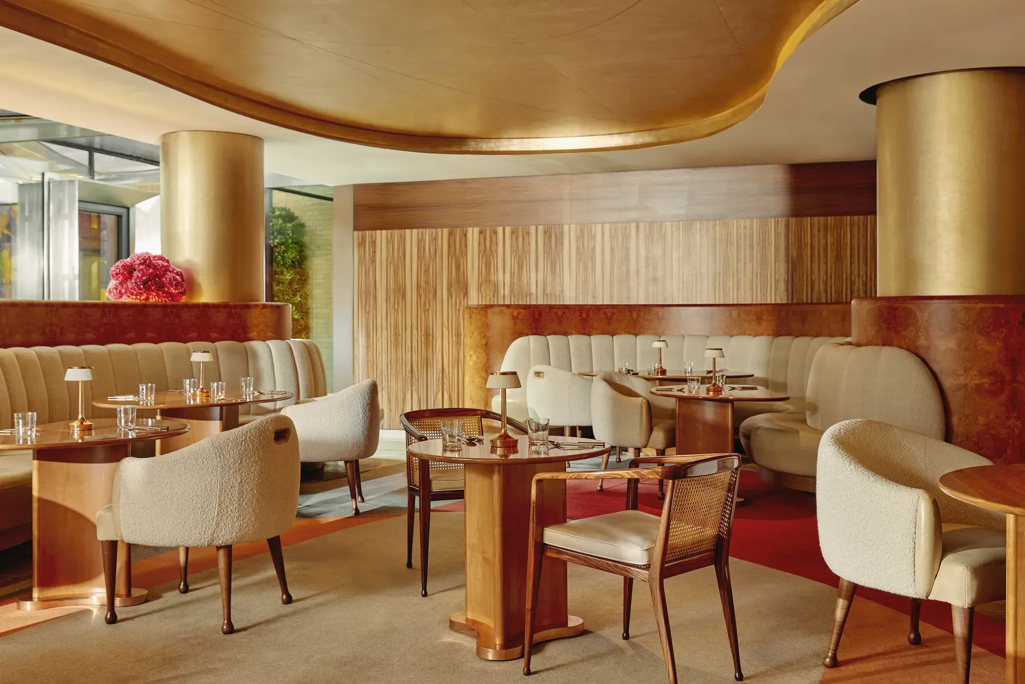 Warm, contemporary café with soft cream seating, wood accents, gold finishes, and intimate table settings.