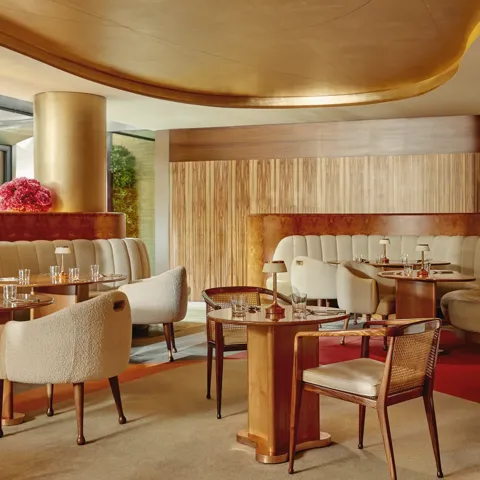 Warm, contemporary café with soft cream seating, wood accents, gold finishes, and intimate table settings.