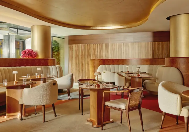 Warm, contemporary café with soft cream seating, wood accents, gold finishes, and intimate table settings.