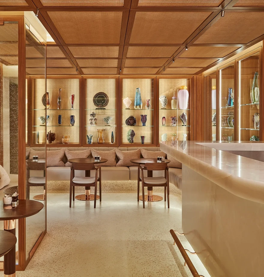Elegant spa café with cushioned seating, marble-topped bar, and backlit shelves displaying an array of decorative glass vases.