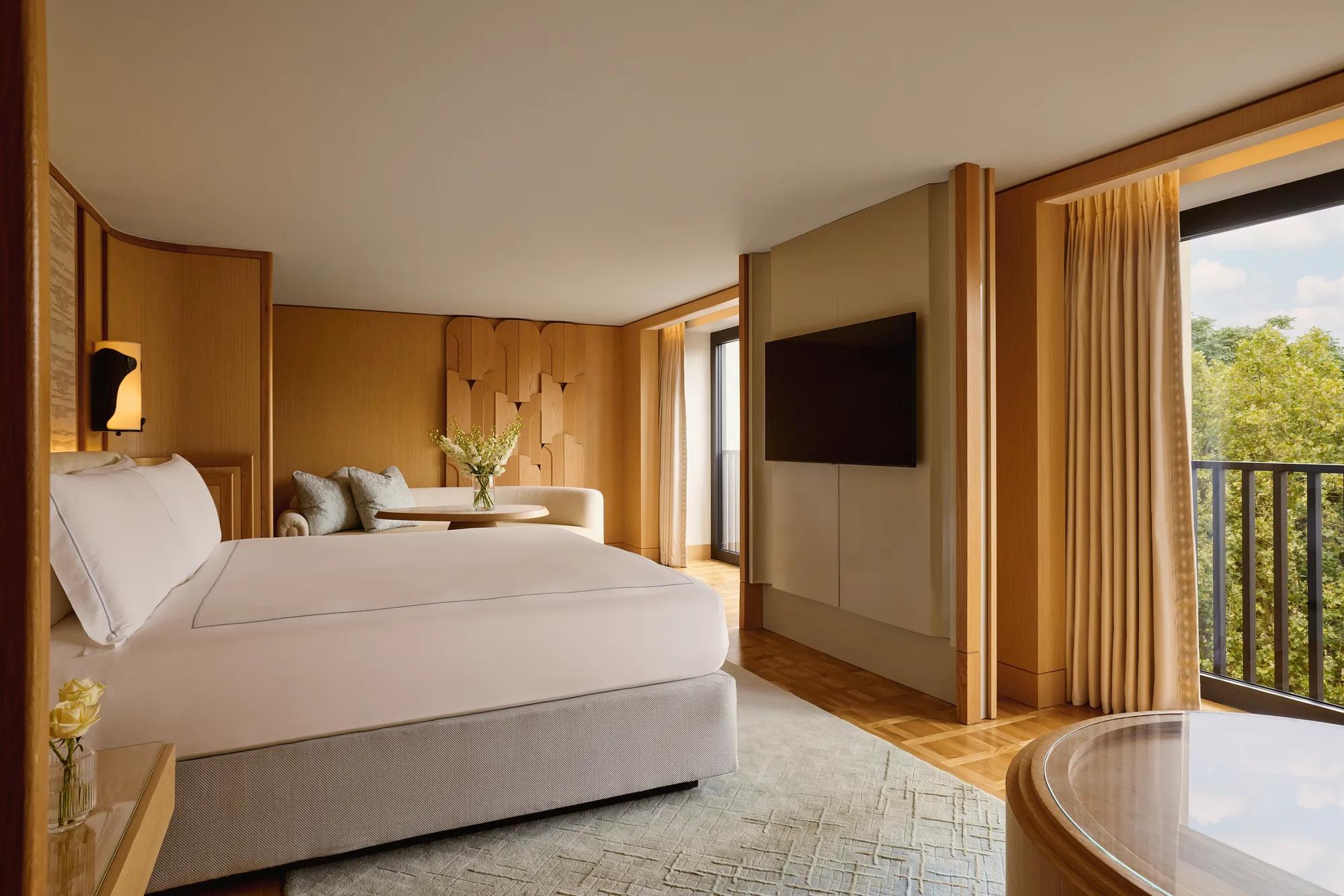 Bedroom with king bed, seating area, flat-screen TV, and balcony overlooking greenery