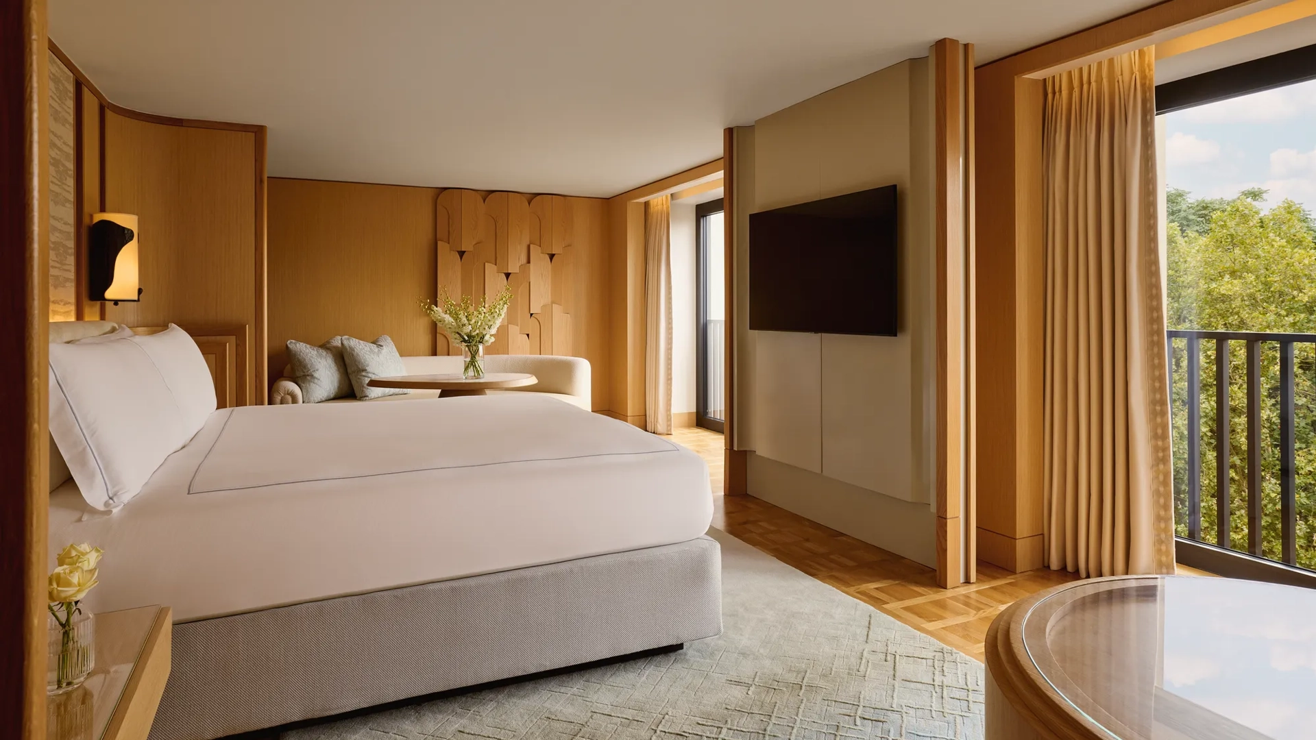 Bedroom with king bed, seating area, flat-screen TV, and balcony overlooking greenery