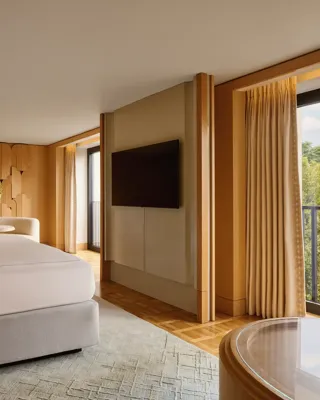 Bedroom with king bed, seating area, flat-screen TV, and balcony overlooking greenery
