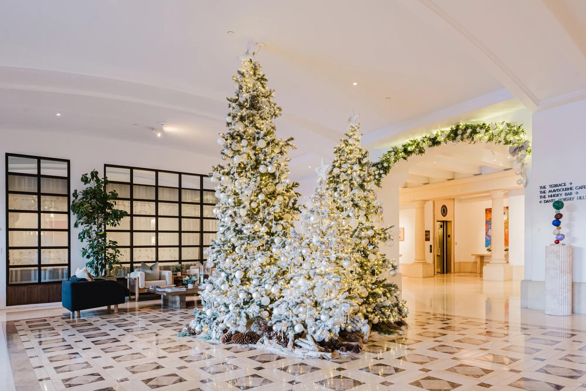 Cluster of decorated Christmas trees with white ornaments and lights in Maybourne Beverly Hills lobby.