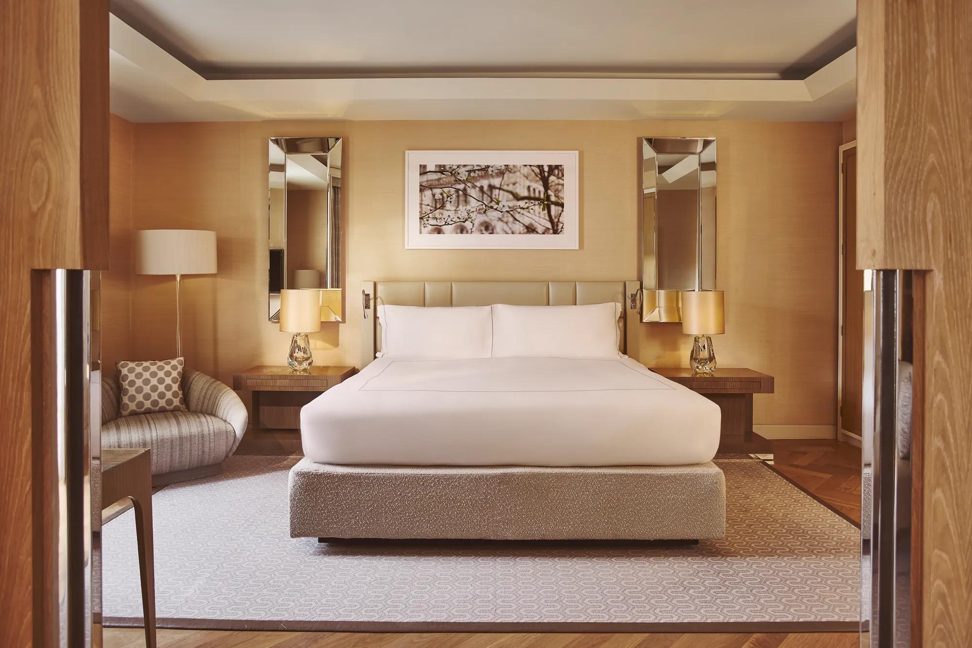 Spacious bedroom with king bed, bedside lamps, armchair, and warm wood-panelled walls.