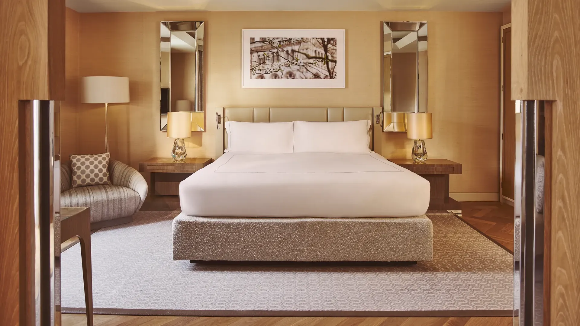 Spacious bedroom with king bed, bedside lamps, armchair, and warm wood-panelled walls.