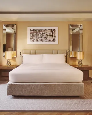 Spacious bedroom with king bed, bedside lamps, armchair, and warm wood-panelled walls.