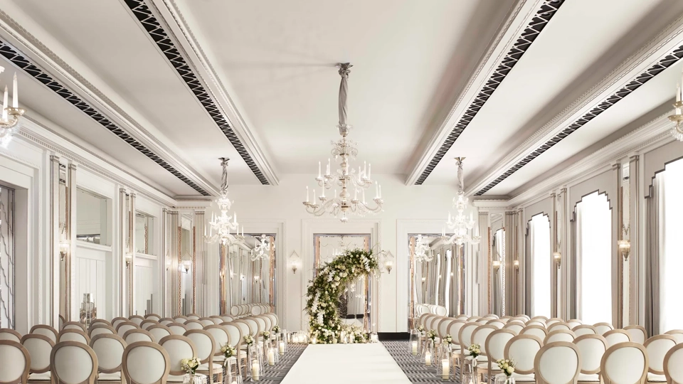 Elegant wedding ceremony room with chandelier lighting, white aisle runner, floral arch, and rows of cream chairs.