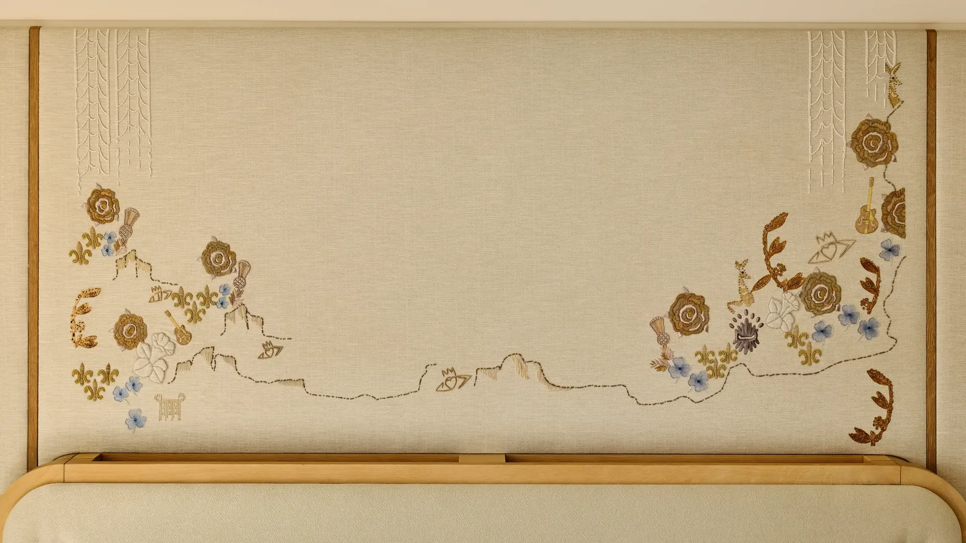Close-up of a decorative embroidered wall panel featuring delicate floral motifs in gold, blue, and cream tones above a light wood headboard.