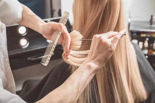 Professional hair stylist trimming long blonde hair during a salon appointment with precision scissors and comb.
