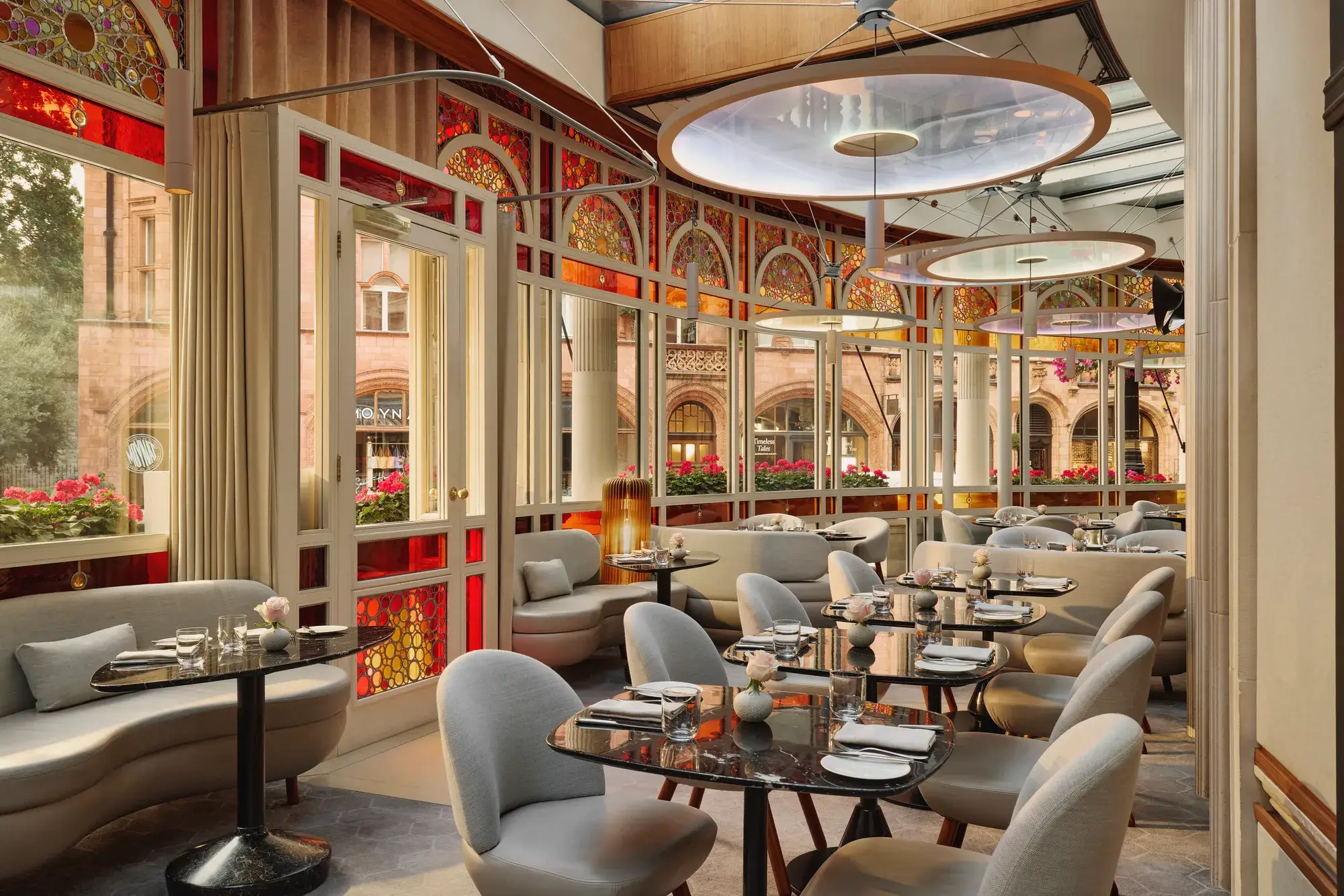 Elegant restaurant with curved banquettes, marble tables, and stained glass windows overlooking a historic street.