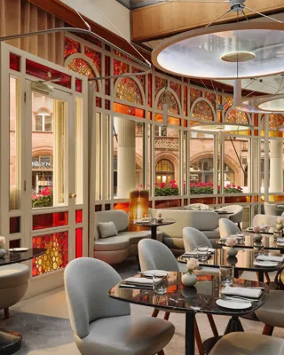 Elegant restaurant with curved banquettes, marble tables, and stained glass windows overlooking a historic street.