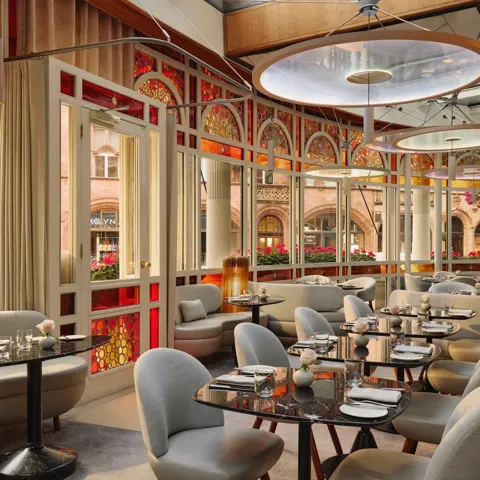 Elegant restaurant with curved banquettes, marble tables, and stained glass windows overlooking a historic street.