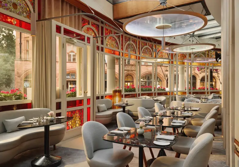 Elegant restaurant with curved banquettes, marble tables, and stained glass windows overlooking a historic street.