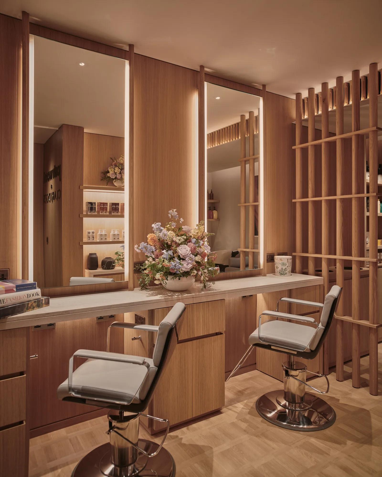 Elegant salon space at Claridge’s featuring two styling chairs, wooden panelling, softly lit mirrors, and a bouquet of flowers on the counter.