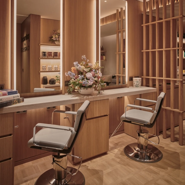 Elegant salon space at Claridge’s featuring two styling chairs, wooden panelling, softly lit mirrors, and a bouquet of flowers on the counter.