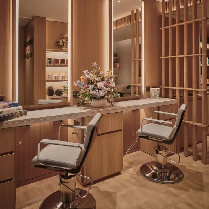 Elegant salon space at Claridge’s featuring two styling chairs, wooden panelling, softly lit mirrors, and a bouquet of flowers on the counter.