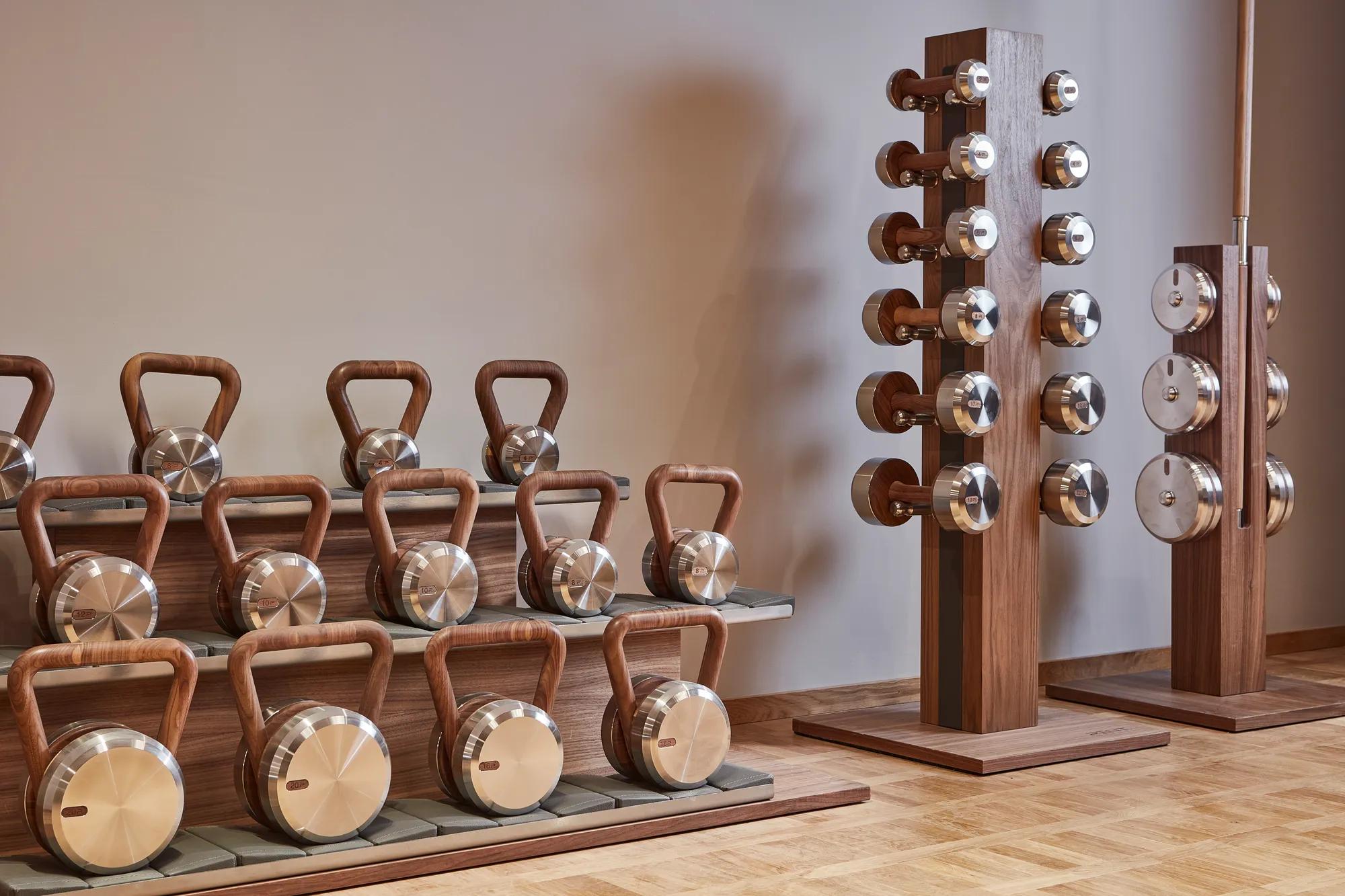 Stylish fitness equipment at The Maybourne Riviera gym, featuring polished metal and wood kettlebells and dumbbells arranged neatly on wooden stands.
