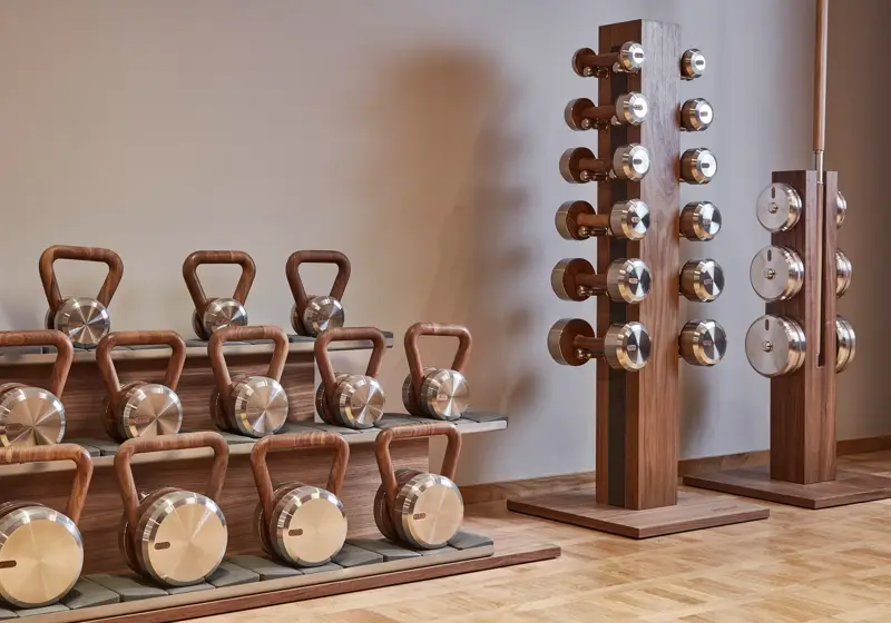 Stylish fitness equipment at The Maybourne Riviera gym, featuring polished metal and wood kettlebells and dumbbells arranged neatly on wooden stands.