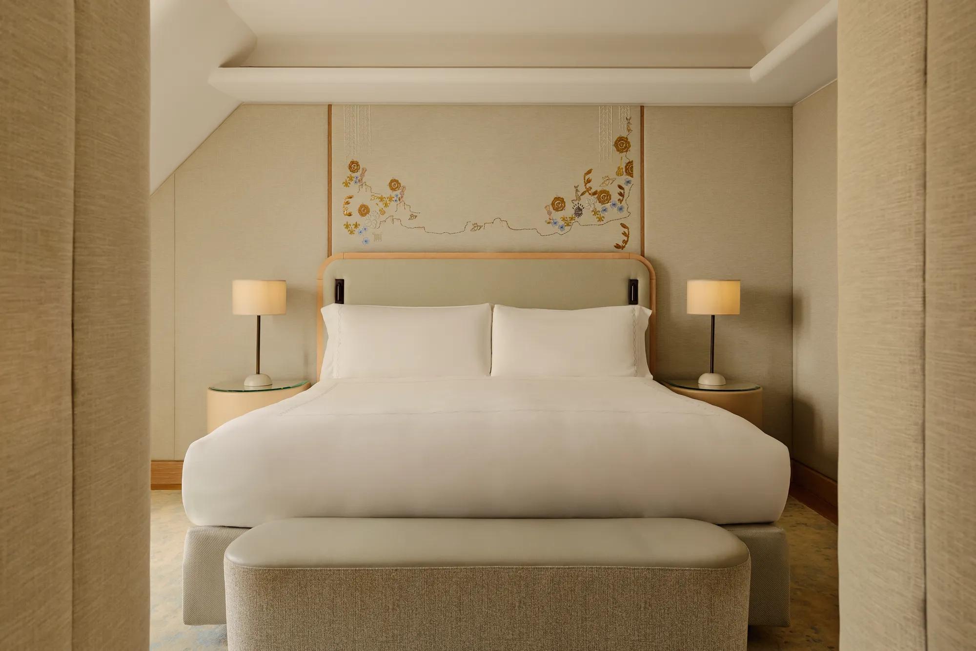 Double bed with white linens, upholstered headboard, bedside lamps, and floral wall art in a calm neutral-toned bedroom