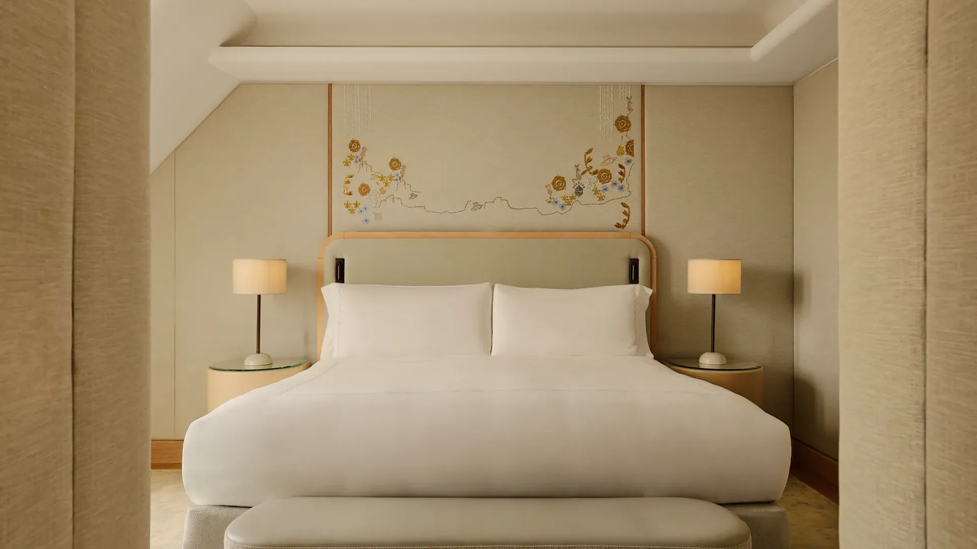 Double bed with white linens, upholstered headboard, bedside lamps, and floral wall art in a calm neutral-toned bedroom
