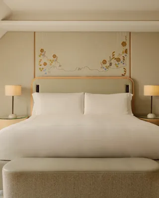 Double bed with white linens, upholstered headboard, bedside lamps, and floral wall art in a calm neutral-toned bedroom
