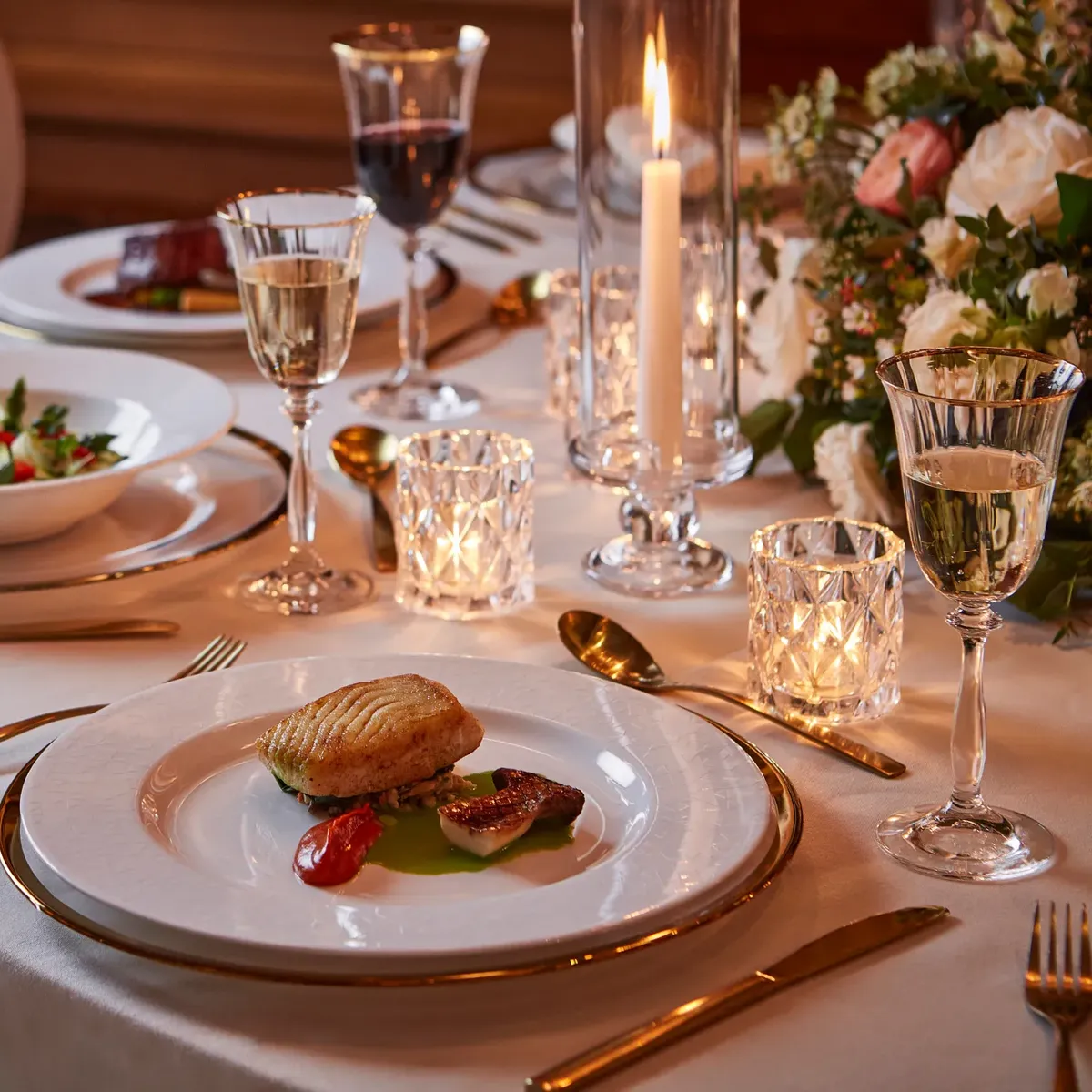Elegant candlelit dinner table with plated fine dining dishes, crystal glasses, and floral centerpiece set for a formal occasion.