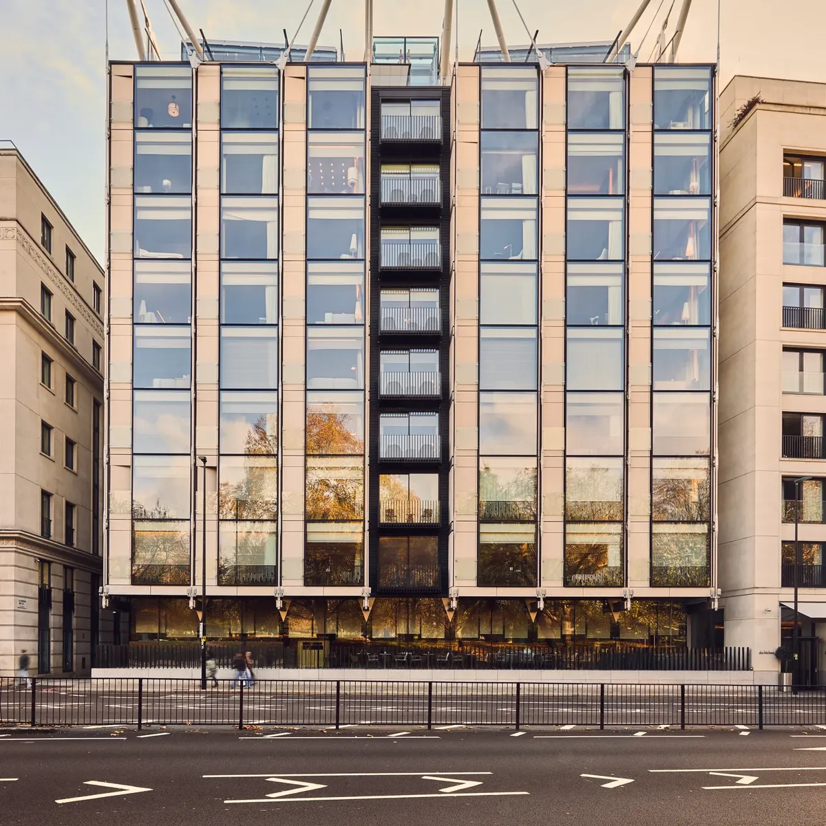 Modern glass-fronted building with vertical window bays and sculptural roof supports, viewed from across a city street.