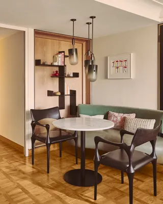 Dining nook with round marble table, two chairs, built-in bench seating, and pendant lights.