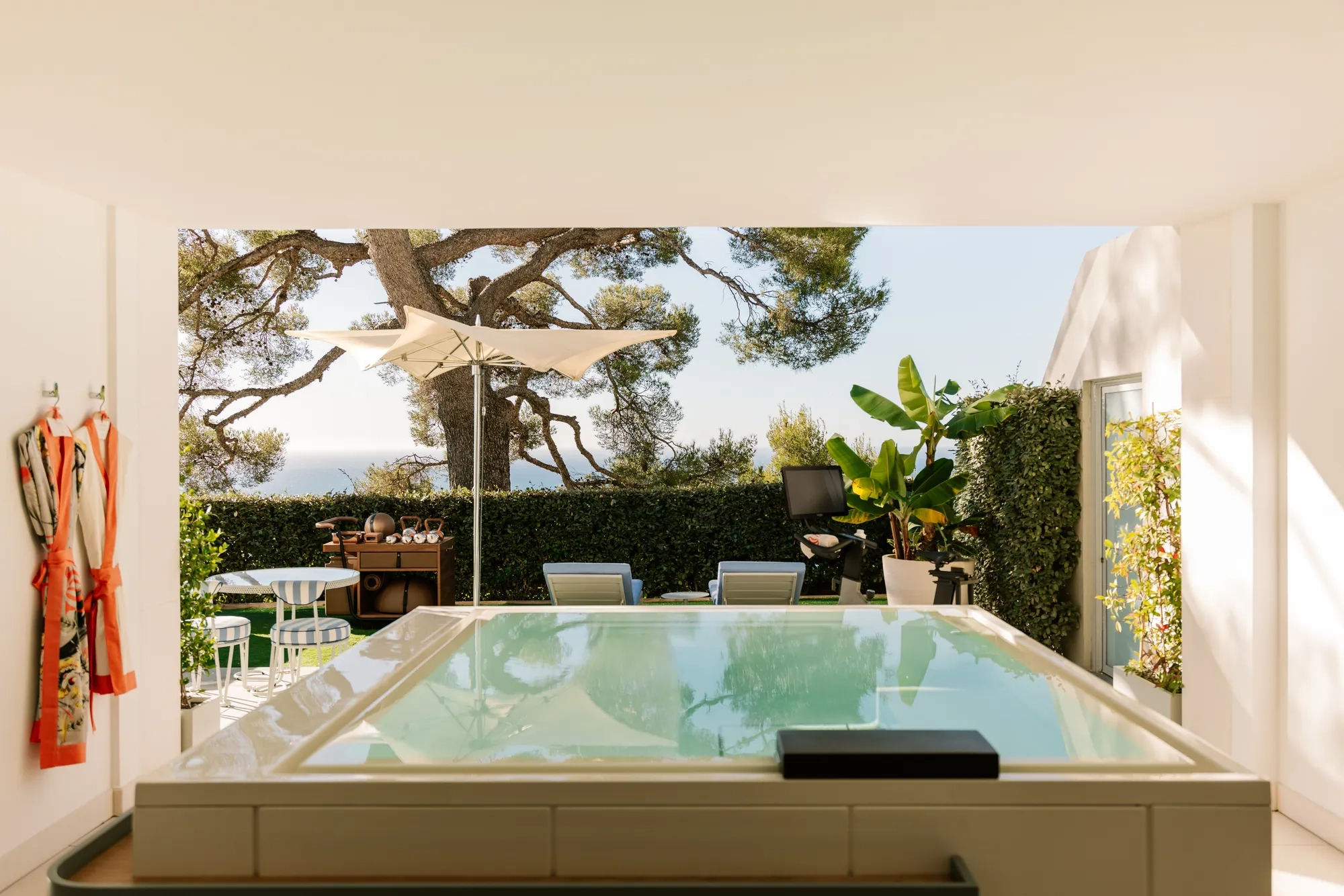 Terrasse privée avec bassin, transats, parasol et jardin avec vue sur la mer.