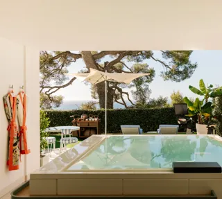 Terrasse privée avec bassin, transats, parasol et jardin avec vue sur la mer.