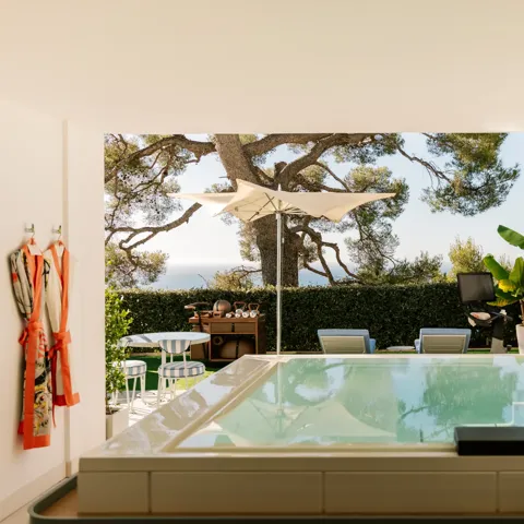 Terrasse privée avec bassin, transats, parasol et jardin avec vue sur la mer.