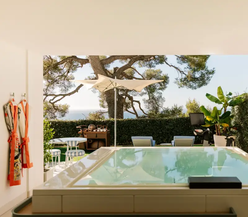 Terrasse privée avec bassin, transats, parasol et jardin avec vue sur la mer.