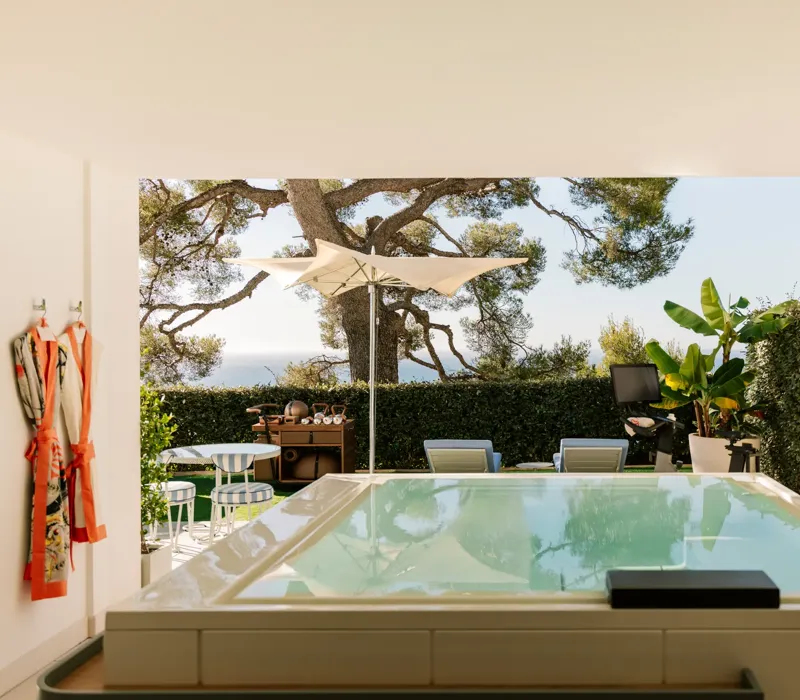 Terrasse privée avec bassin, transats, parasol et jardin avec vue sur la mer.