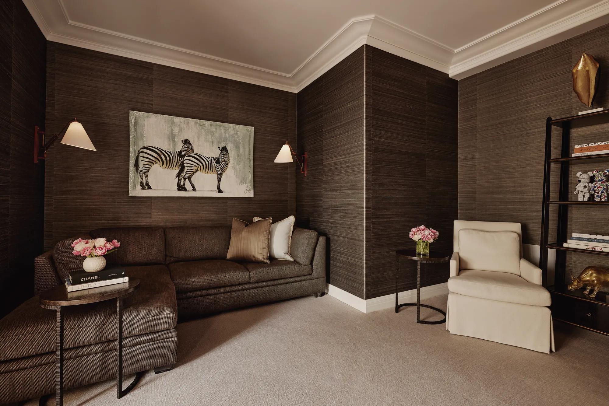 Den or theatre room in Maybourne Beverly Hills three bedroom residence with sectional sofa, armchair, zebra artwork, bookshelves, and side tables.