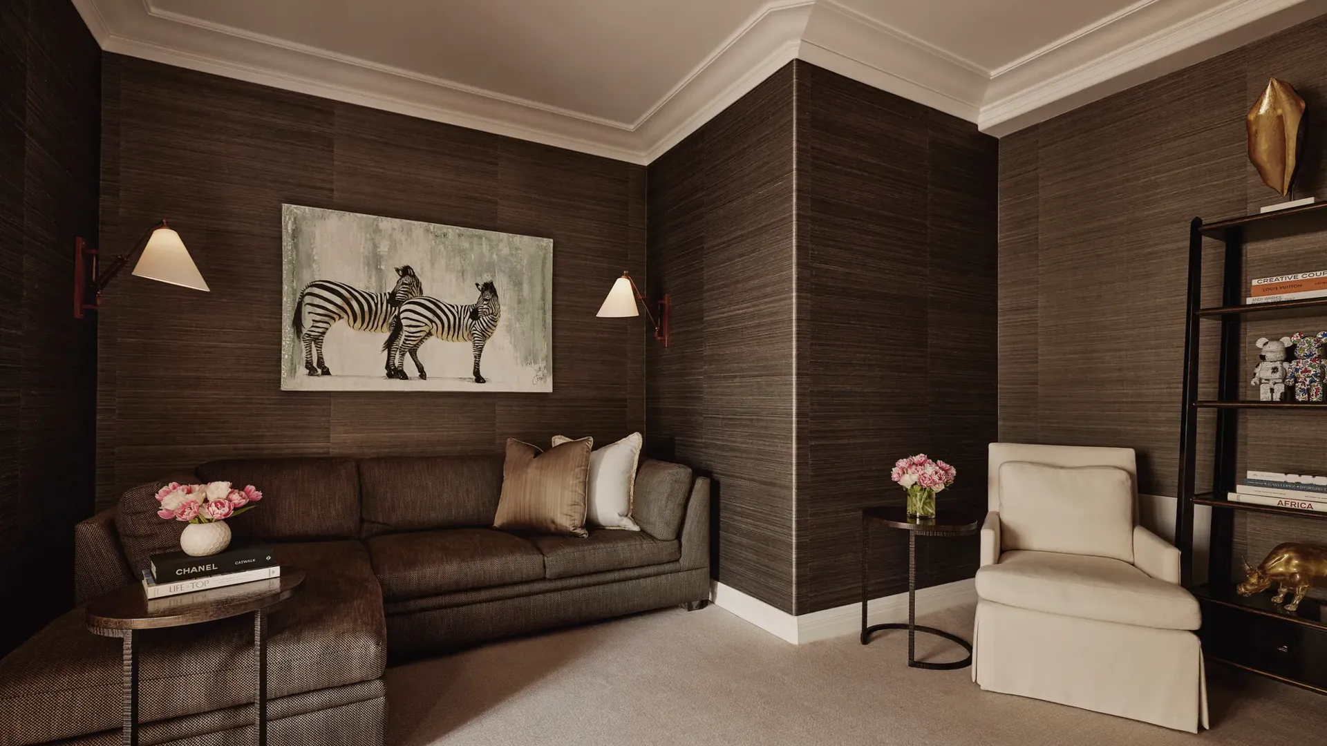 Den or theatre room in Maybourne Beverly Hills three bedroom residence with sectional sofa, armchair, zebra artwork, bookshelves, and side tables.