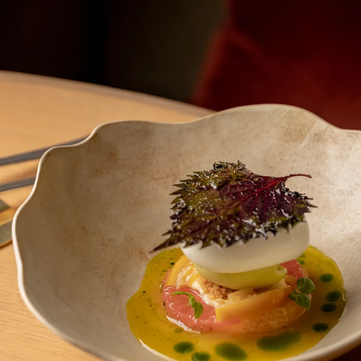 Plated gourmet dish with layered vegetables, creamy topping and crisp leaf garnish in a shallow ceramic bowl