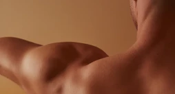 Close-up of a man’s bare back and shoulder with arm extended, lit in warm amber tones