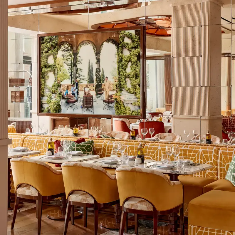 Dining area with yellow upholstered chairs and a large framed photograph of an outdoor terrace scene.