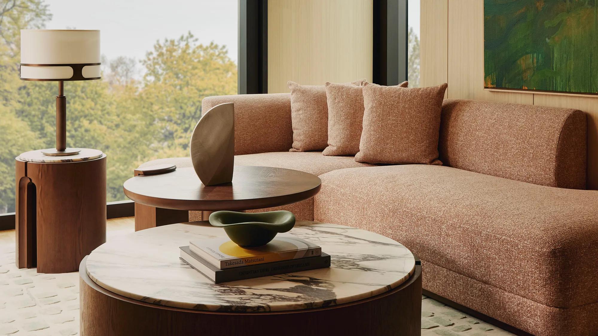 Modern living room with a neutral sectional sofa, large window overlooking green trees.