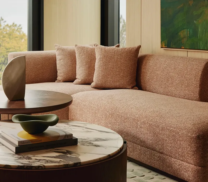 Modern living room with a neutral sectional sofa, large window overlooking green trees.